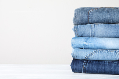 Stack of different jeans on white wooden table. Space for text