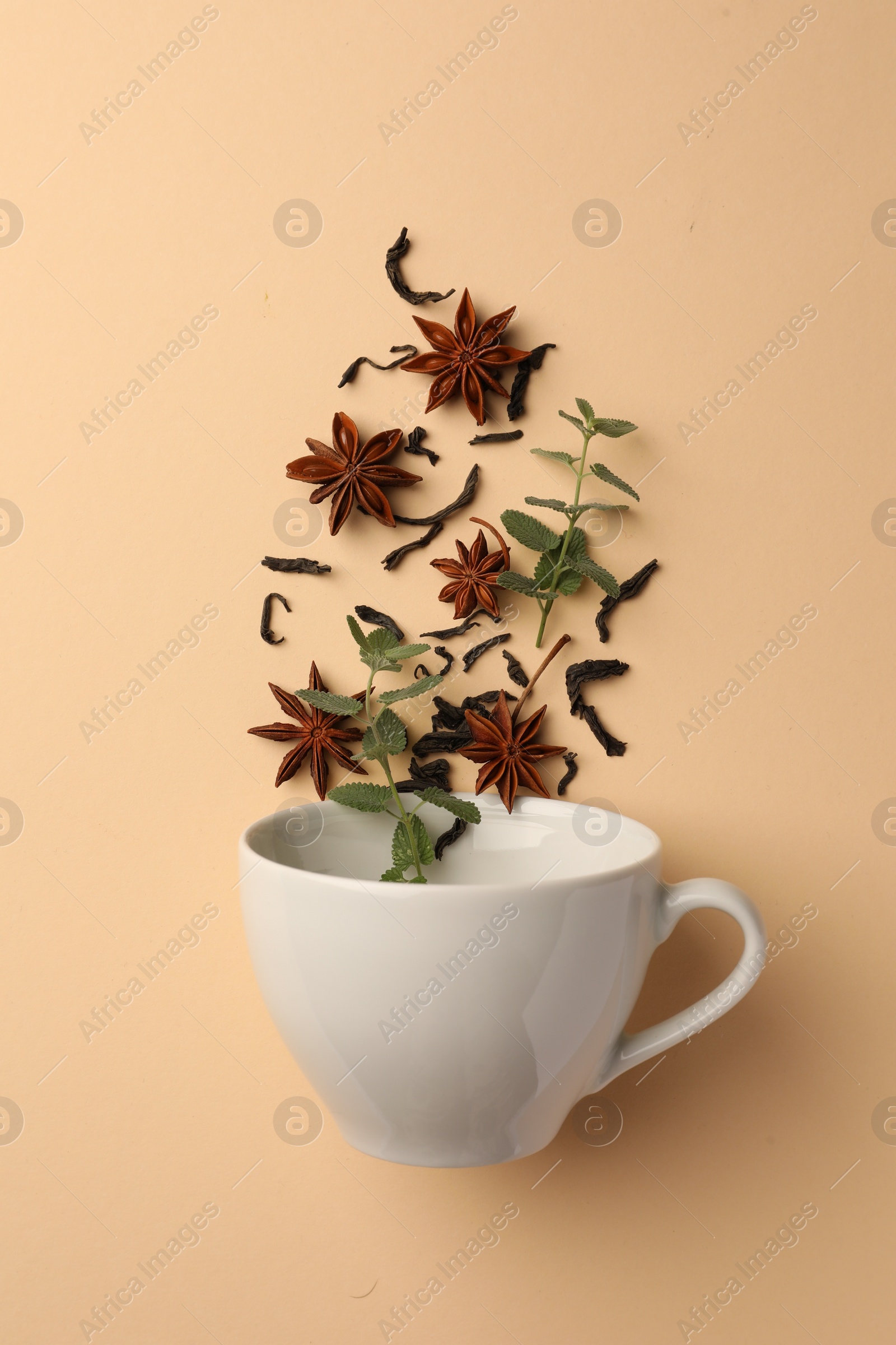 Photo of Anise stars, dry tea and mint falling into cup on beige background, flat lay