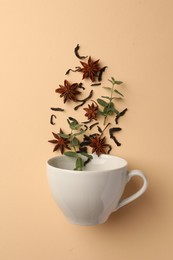 Anise stars, dry tea and mint falling into cup on beige background, flat lay