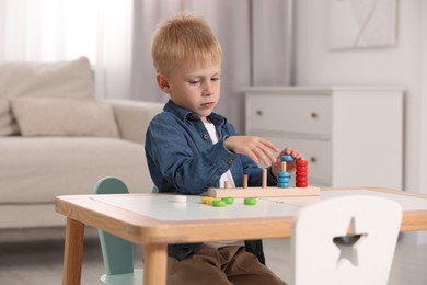 Photo of Cute little boy playing with stacking and counting game at table indoors. Child's toy