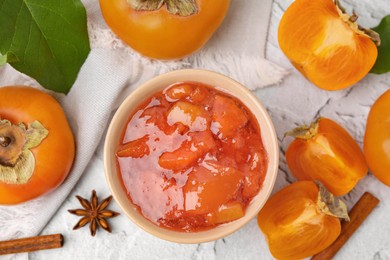 Photo of Bowl of tasty persimmon jam and ingredients on white textured table, flat lay