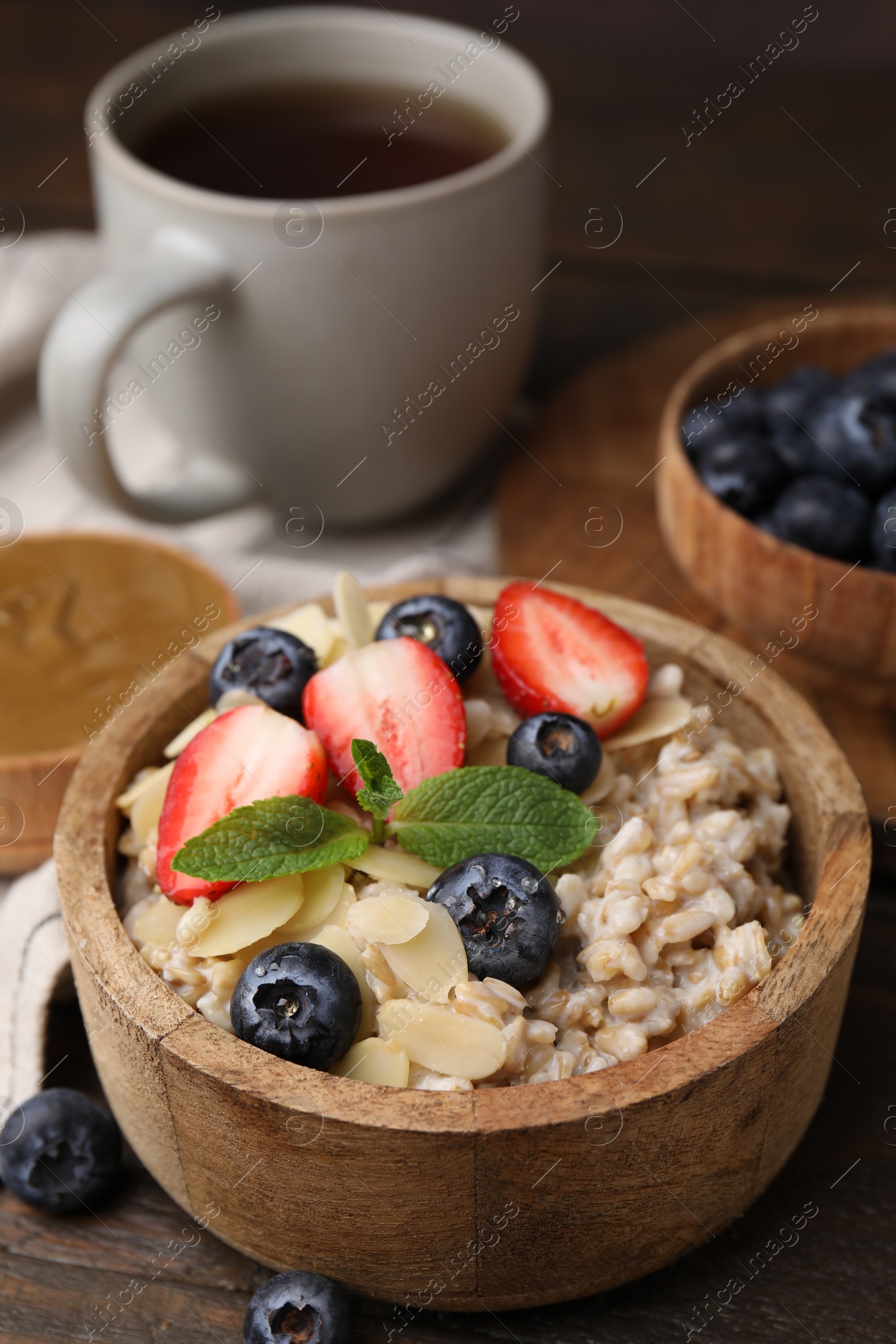 Photo of Tasty oatmeal with strawberries, blueberries and almond petals in bowl on wooden table