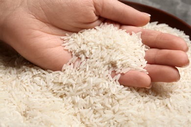 Photo of Woman holding grains near plate with rice on table, closeup