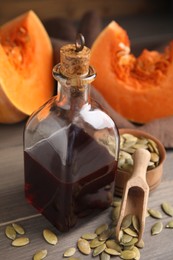 Photo of Glass bottle of oil with cut pumpkin and seeds on wooden table, closeup
