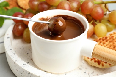 Photo of Dipping grape into fondue pot with chocolate on tray