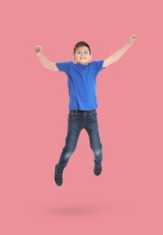 Happy boy jumping on pink background, full length portrait