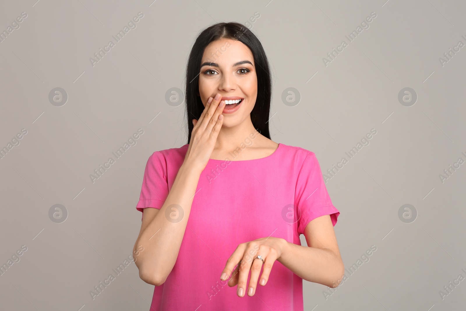 Photo of Happy young woman wearing beautiful engagement ring on grey background