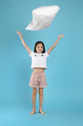 Photo of Cute girl in pajamas throwing up pillow on light blue background