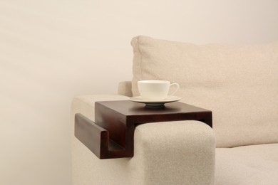 Cup of coffee on sofa with wooden armrest table indoors. Interior element