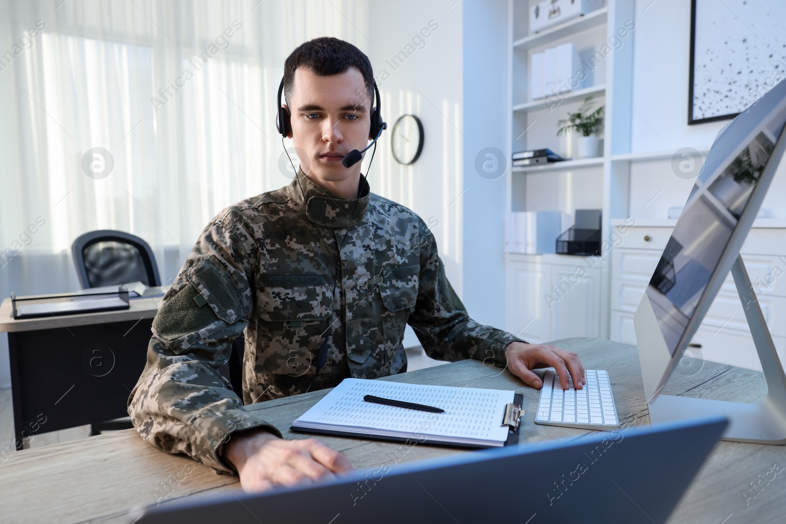 Photo of Military service. Young soldier in headphones working at wooden table in office