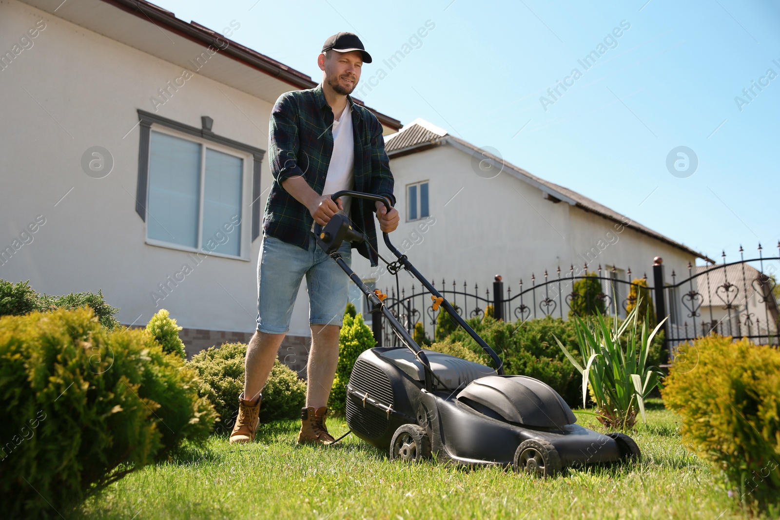 Photo of Man cutting green grass with lawn mower in garden