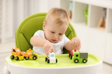 Photo of Children toys. Cute little boy playing with toy cars in high chair at home