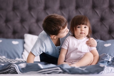 Photo of Cute little boy with his baby sister on bed at home