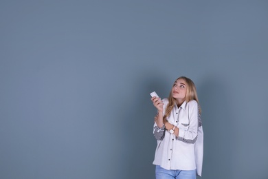 Young woman operating air conditioner with remote control on color background