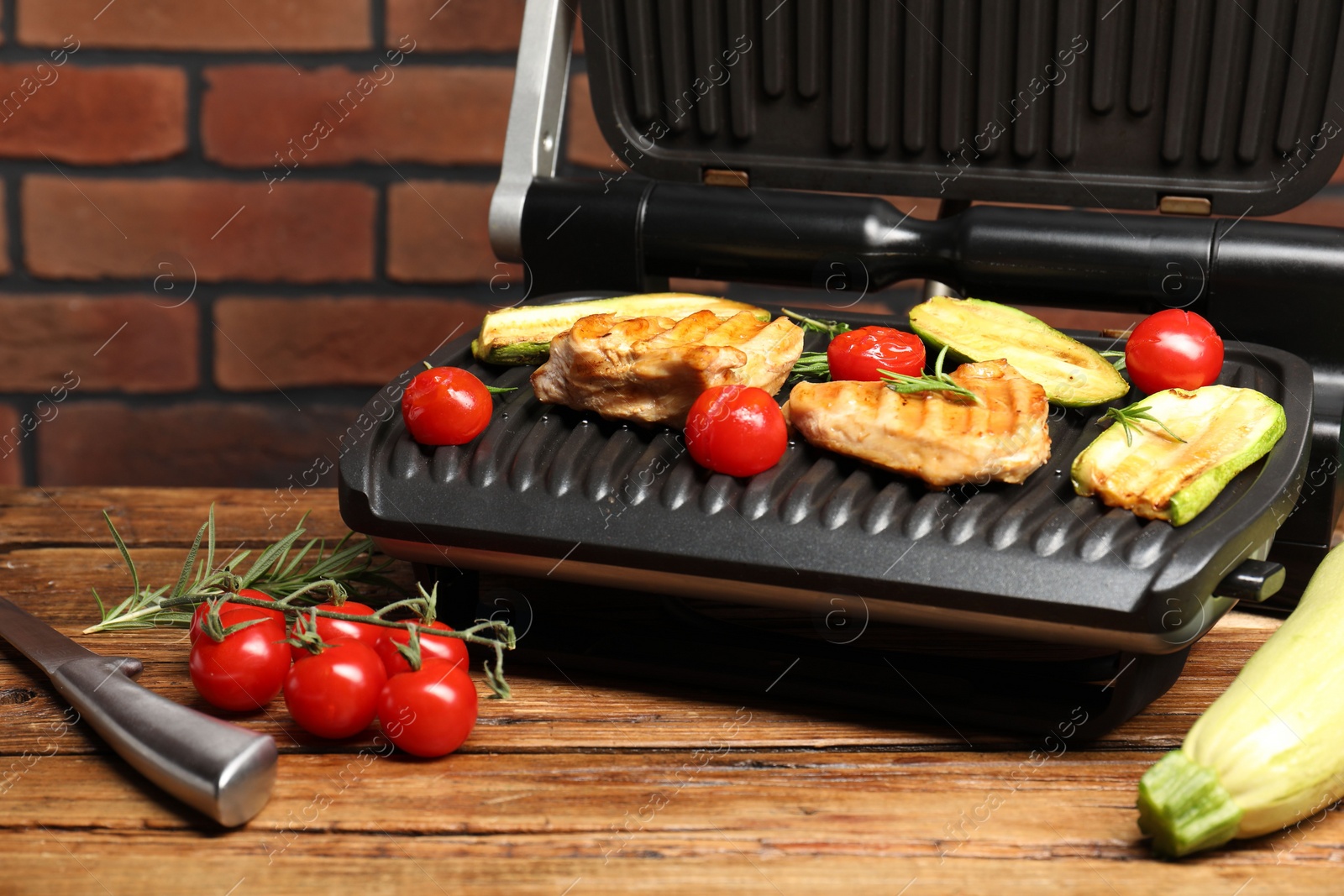 Photo of Electric grill with tasty meat, rosemary and vegetables on wooden table