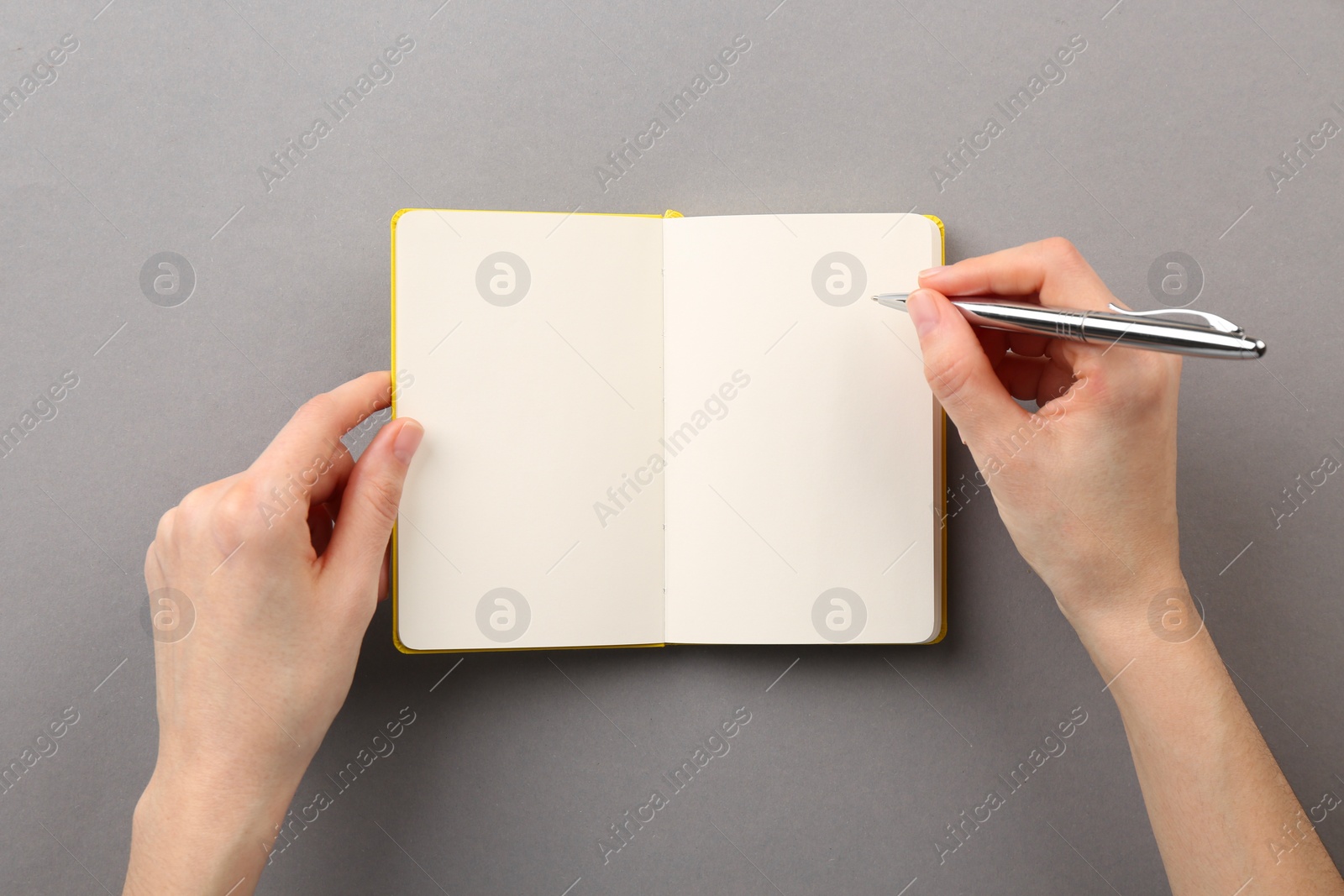 Photo of Woman writing in notebook on grey background, top view