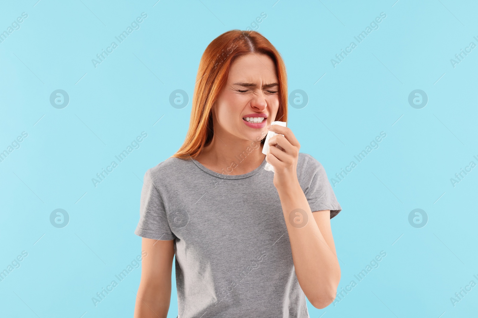 Photo of Suffering from allergy. Young woman with tissue sneezing on light blue background