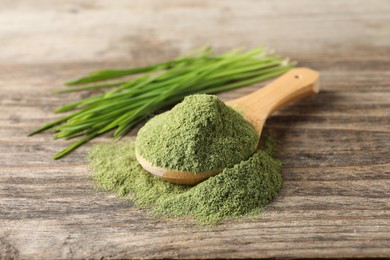 Photo of Wheat grass powder in spoon on wooden table, closeup