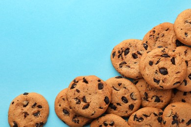 Many delicious chocolate chip cookies on light blue background, flat lay. Space for text