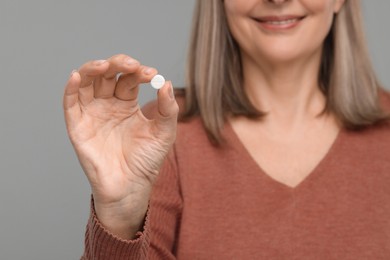 Senior woman with pill on grey background, closeup