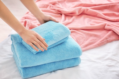 Photo of Woman folding clean towels on bed, closeup