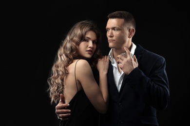 Passionate woman and handsome man using perfume on black background