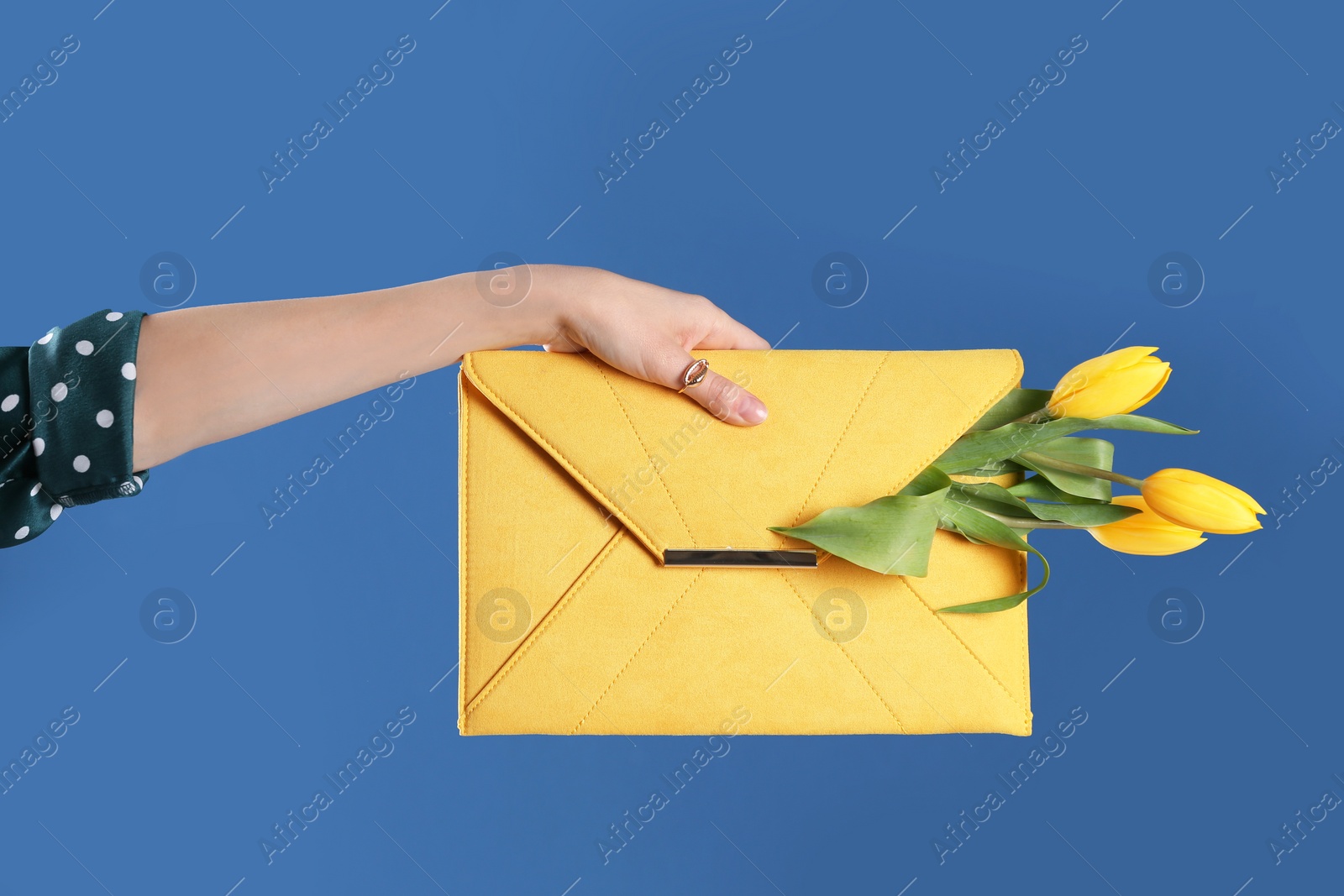 Photo of Woman holding elegant clutch with spring flowers on blue background, closeup