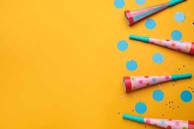 Flat lay composition with party noisemakers and confetti on orange background, space for text