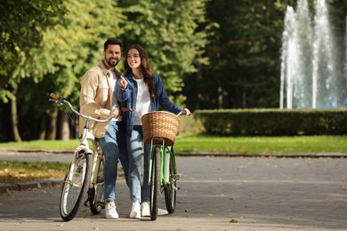 Photo of Beautiful couple with bicycles spending time together in park, space for text
