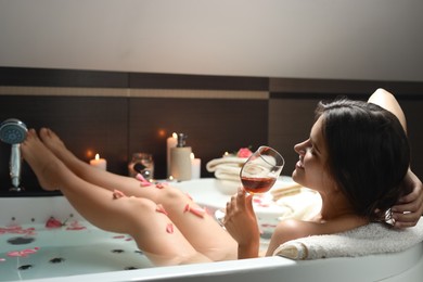 Photo of Woman holding glass of wine while taking bath with rose petals. Romantic atmosphere