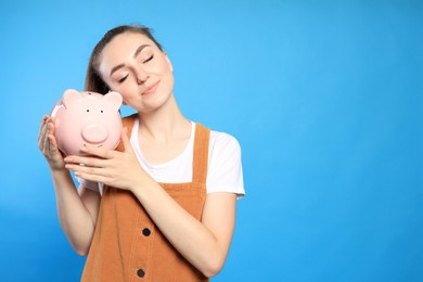 Photo of Happy young woman with piggy bank on light blue background. Space for text