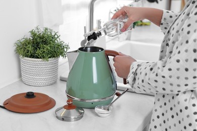 Woman pouring vinegar from bottle into electric kettle in kitchen, closeup