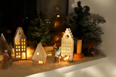 Christmas atmosphere. Beautiful glowing houses, fir trees and toys on window sill indoor