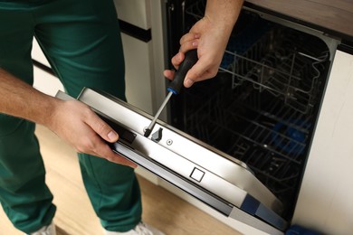 Serviceman repairing dishwasher door with screwdriver indoors, closeup