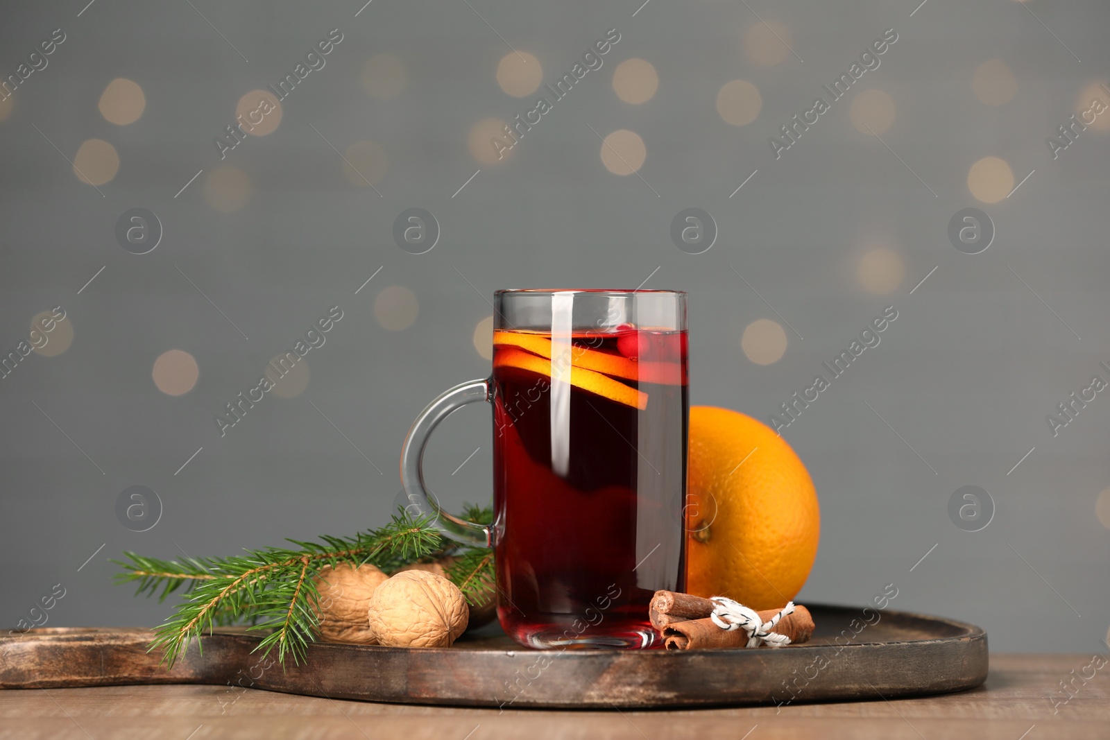 Photo of Aromatic mulled wine in glass cup on wooden table against grey background with blurred lights