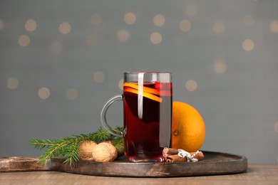 Photo of Aromatic mulled wine in glass cup on wooden table against grey background with blurred lights