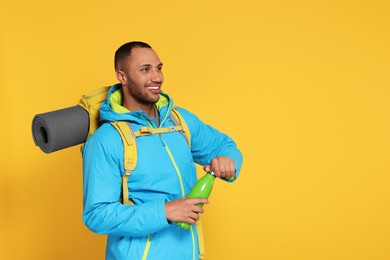 Happy tourist with backpack and thermo bottle on yellow background, space for text