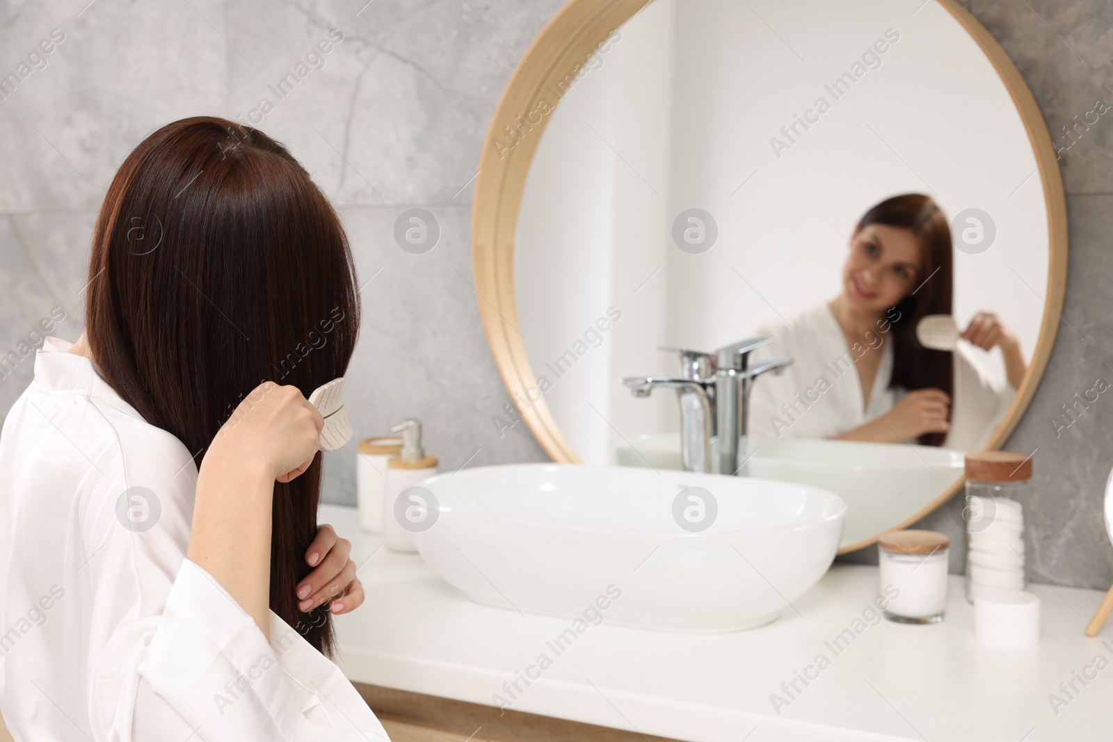 Photo of Beautiful woman brushing her hair near mirror in bathroom, space for text