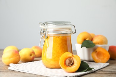 Photo of Jar of apricot jam and fresh fruits on wooden table