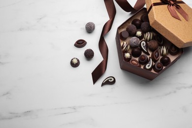 Photo of Open box of delicious chocolate candies and brown ribbon on white marble table, flat lay. Space for text