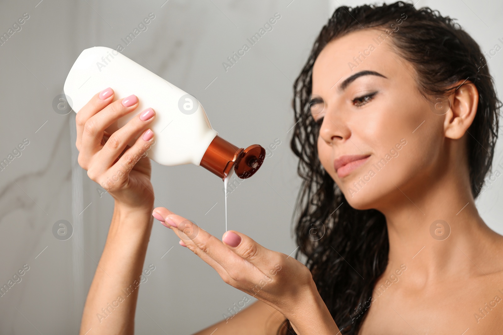 Image of Beautiful young woman with bottle of shampoo in shower at home