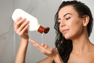 Beautiful young woman with bottle of shampoo in shower at home