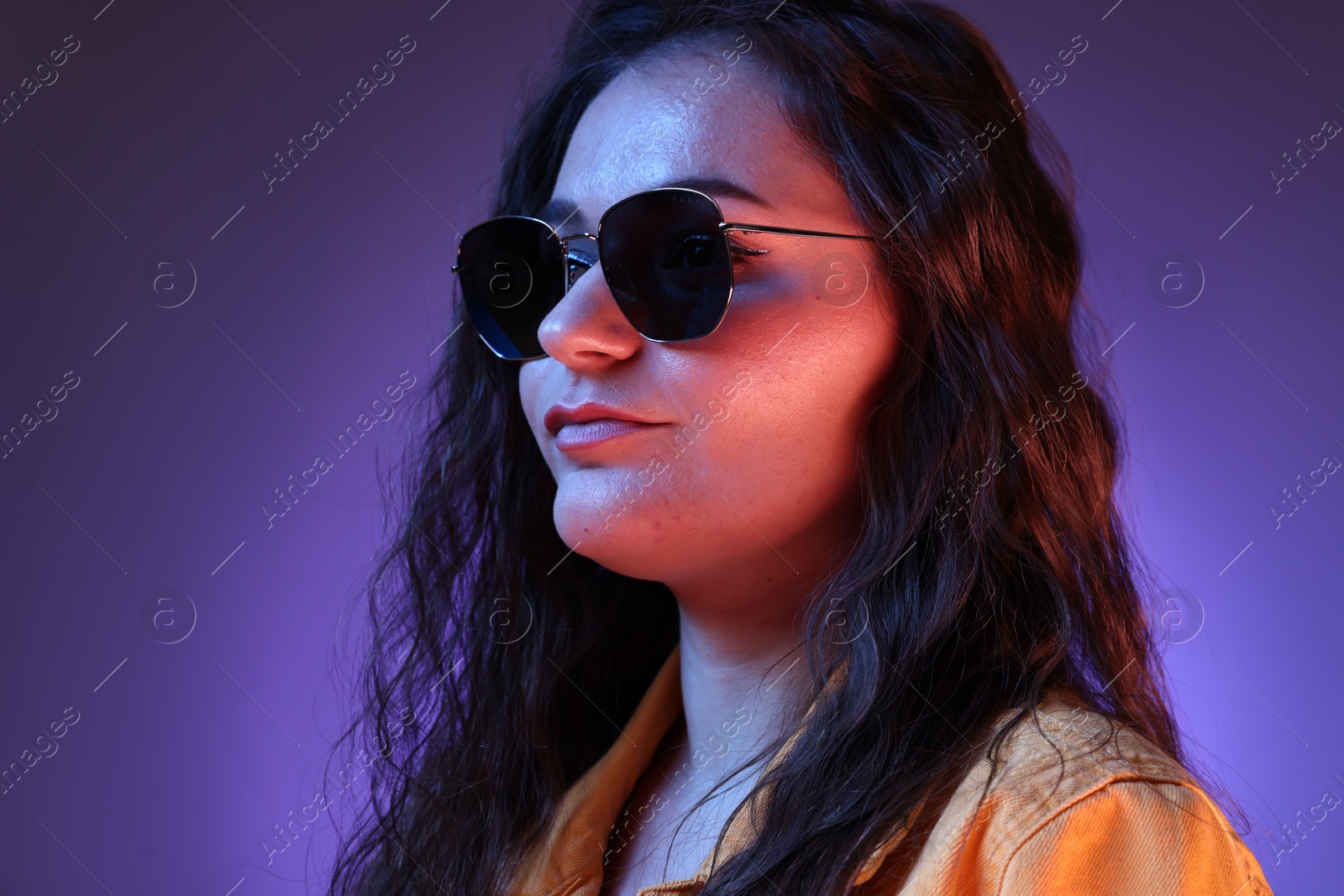 Photo of Portrait of beautiful young woman with stylish sunglasses on color background with neon lights