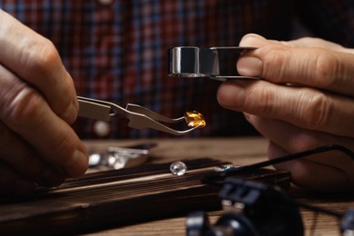 Photo of Professional jeweler working with gemstone at wooden table, closeup