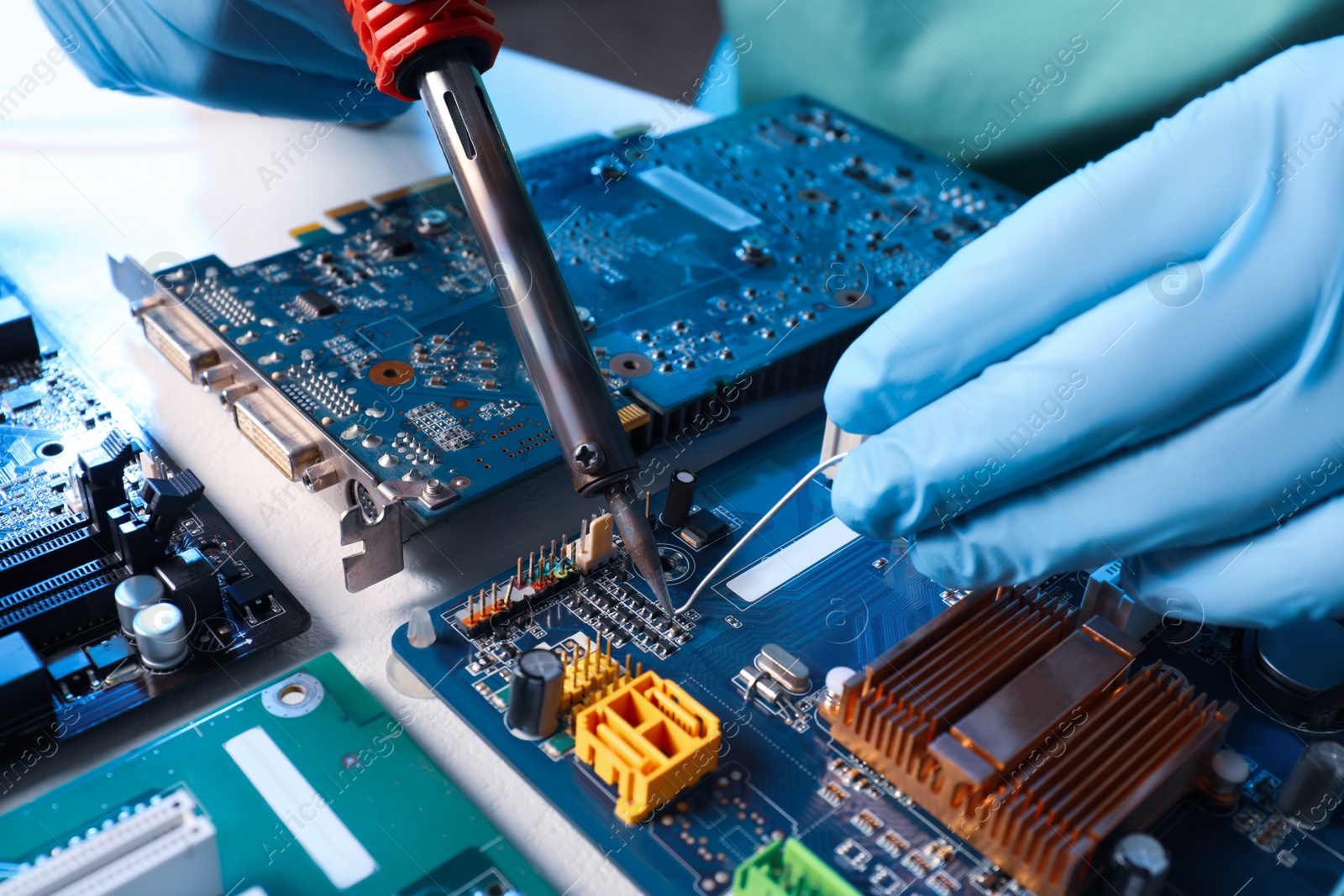 Photo of Technician repairing electronic circuit board with soldering iron at table, closeup