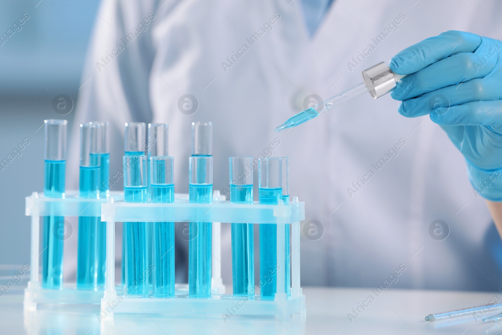 Photo of Scientist dripping liquid from pipette into test tube on blurred background, closeup