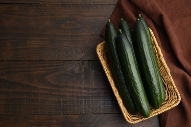 Photo of Fresh cucumbers in wicker basket on wooden table, top view. Space for text