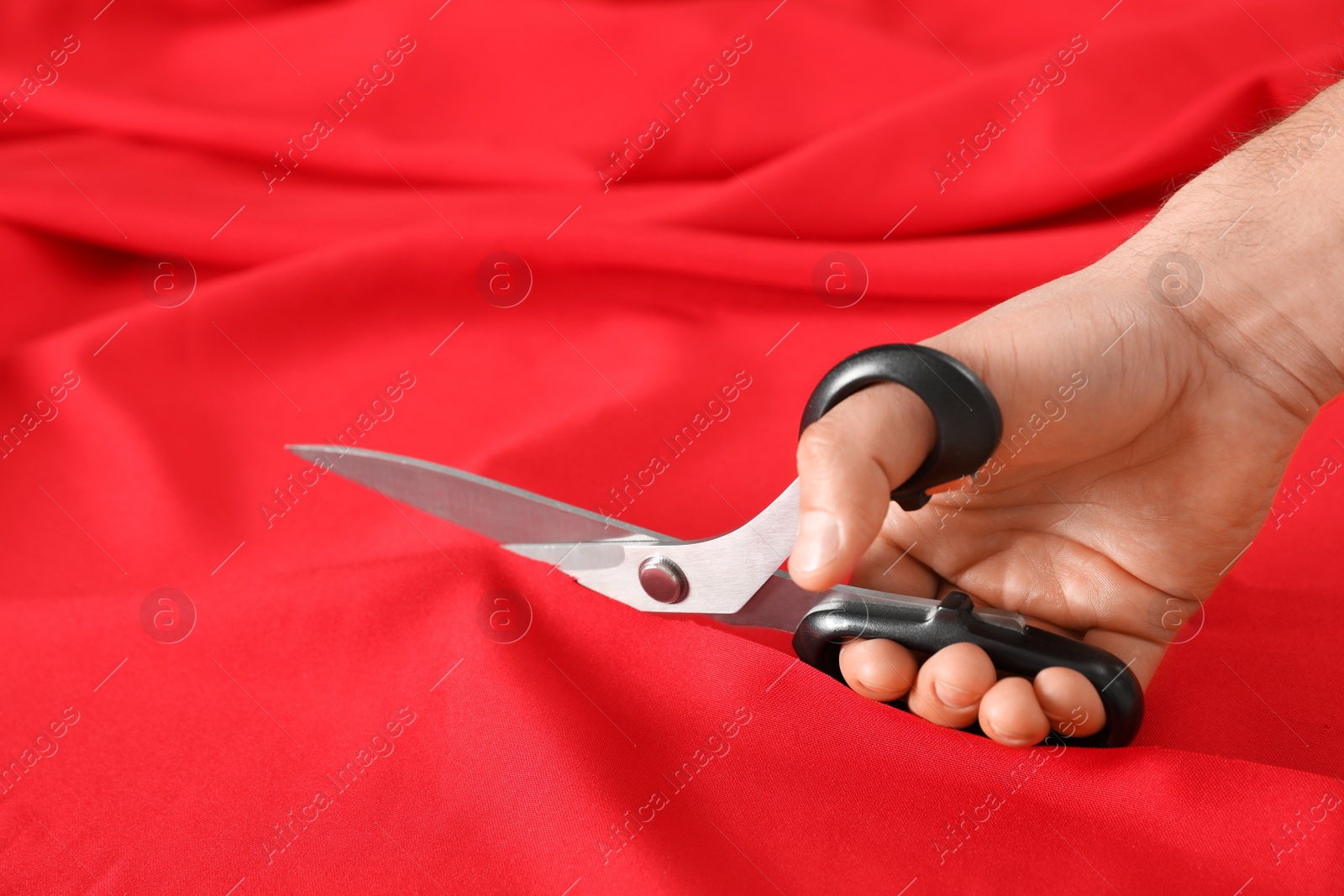 Photo of Professional tailor cutting red fabric with scissors in workshop, closeup