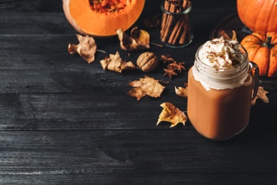 Photo of Delicious pumpkin latte on black wooden table. Space for text