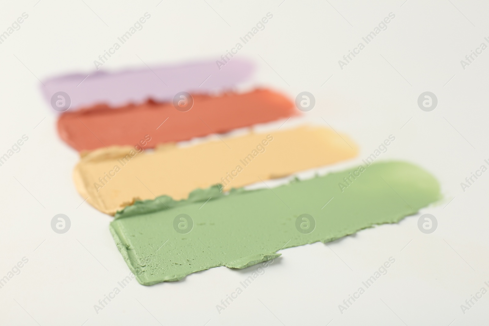 Photo of Samples of different color correcting concealers on white background, closeup